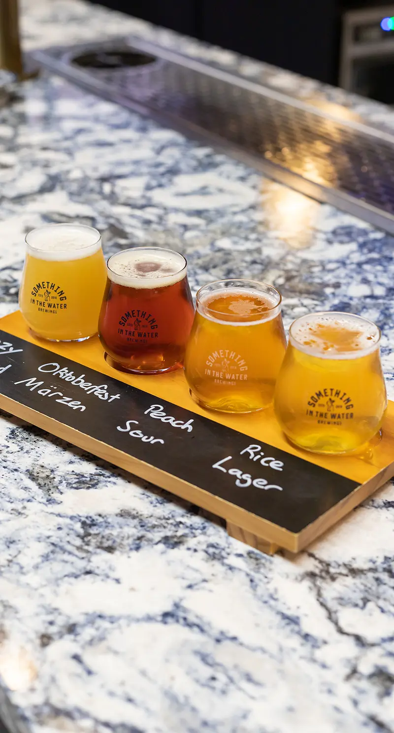 Flight of four craft beers on a wooden paddle on the marble bar at the Something in the Water taproom, Kingston